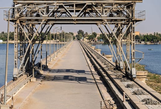 Road across old Esna dam and lock across the Nile River with sandy hills of Sahara desert behind