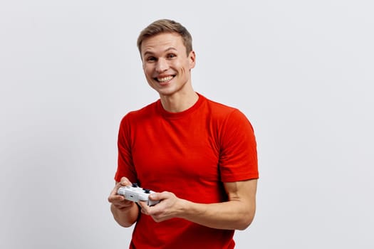 smiling man in red t-shirt holding game controller facing camera expressing happiness and engagement in digital entertainment concept. casual young caucasian man enjoying leisure time, technology and relaxation focus. Concept: digital entertainment