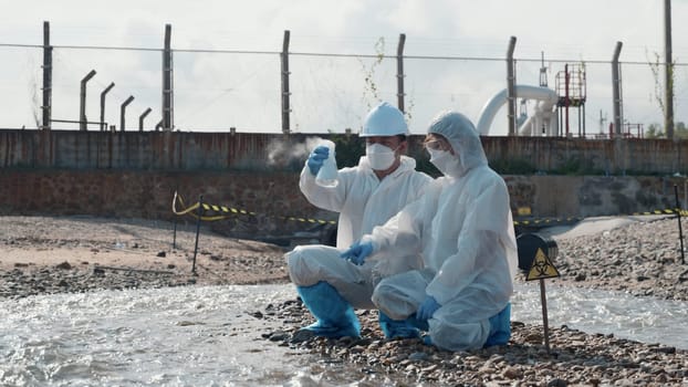 Ecologist sampling water toxic chemicals from river with test tube glass and have white smoke, Biologist wear protective suit and mask collects sample waste water from industrial, problem environment