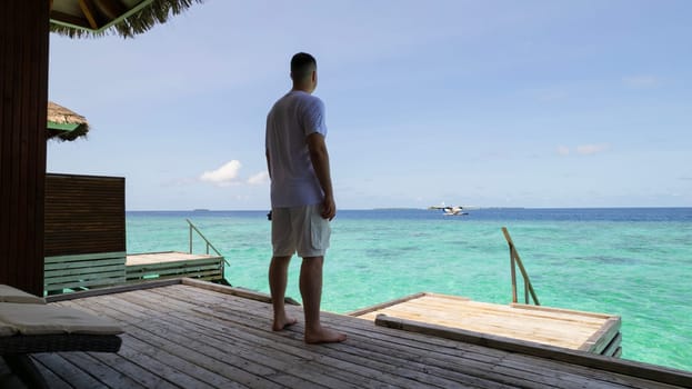 A guy in white clothes admires the turquoise ocean. Vacation in the Maldives. He looks into the future and enjoys it. Small waves. Descent into the water. Wooden villa. Bungalows on the water