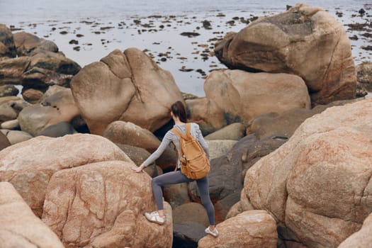 Adventurous female model in athletic wear climbing rocky shoreline, radiating an active lifestyle and connection with nature, perfect for outdoor enthusiasts