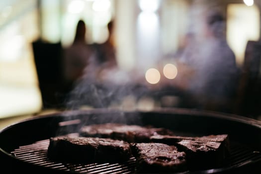 Close-up photo of delicious meat being grilled. In the background, friends and family are sitting and waiting for a meal