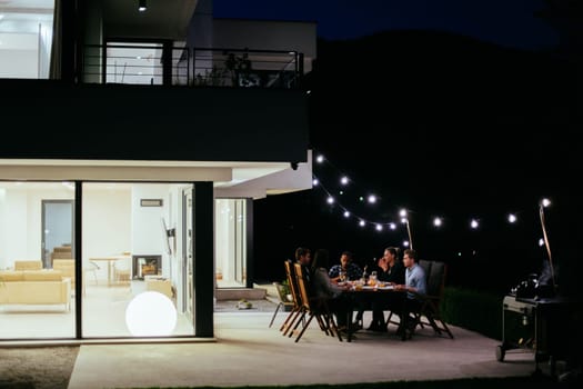 A group of young diverse people having dinner on the terrace of a modern house in the evening. Fun for friends and family. Celebration of holidays, weddings with barbecue.
