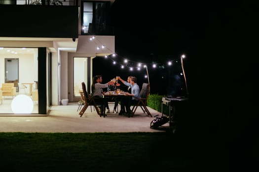 A group of young diverse people having dinner on the terrace of a modern house in the evening. Fun for friends and family. Celebration of holidays, weddings with barbecue.