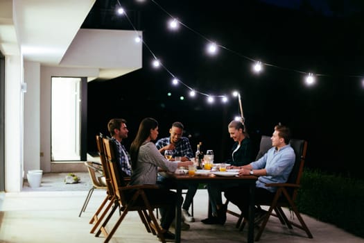 A group of young diverse people having dinner on the terrace of a modern house in the evening. Fun for friends and family. Celebration of holidays, weddings with barbecue.