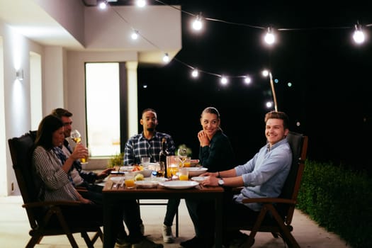 A group of young diverse people having dinner on the terrace of a modern house in the evening. Fun for friends and family. Celebration of holidays, weddings with barbecue.