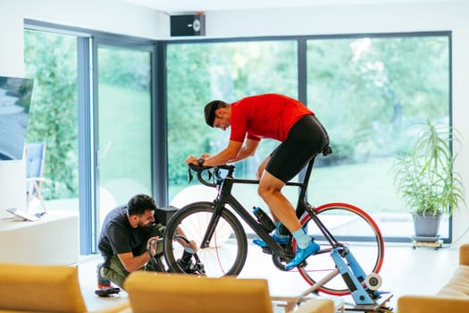 A cameraman filming an athlete riding a triathlon bike on a simulation machine in a modern living room. Training in pandemic conditions