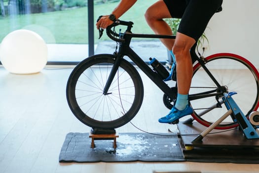 A triathlete riding a triathlon bike on a machine simulation in a modern living room. Training during pandemic conditions