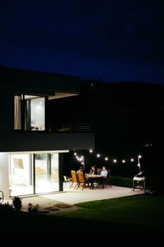 A group of young diverse people having dinner on the terrace of a modern house in the evening. Fun for friends and family. Celebration of holidays, weddings with barbecue.