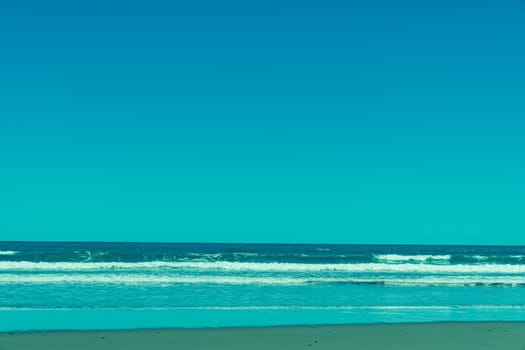 Opunake surf beach in retro with west coast black sand, blue sky and water.