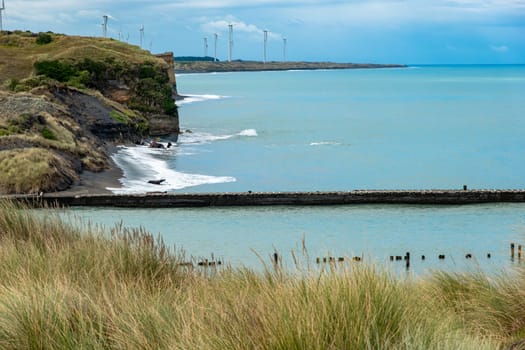Sheer coastal cliffs just south of Patea with wind turbines generating renewable energy in distance, New Zealand.