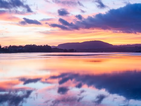 Intensity of sky and reflections in calm water in blue hour sunrise over bay in Tauranga New Zealand.