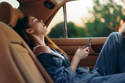 A young woman in casual denim attire, enjoying a moment of solitude in a car, looking at her phone with a serene expression, illuminated by gentle evening light.