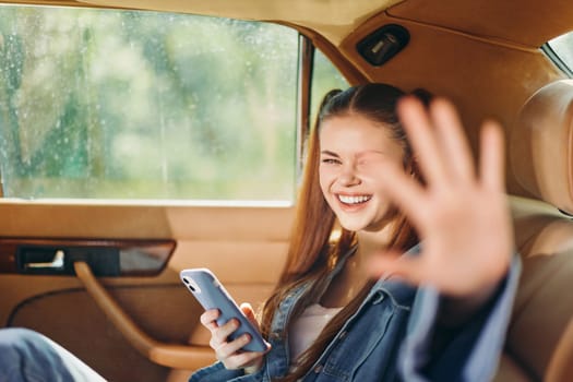Happy girl in a car, engaging with her smartphone, radiating positivity and enthusiasm. The sunny background complements her vibrant mood, ideal for lifestyle concepts.