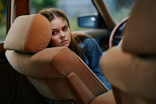 A young woman, dressed casually, appears contemplative and sad as she leans against the seat of a vintage car. The soft color palette and blurred background evoke nostalgia and introspection, making