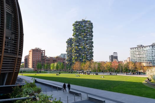 Milan, Italy - April, 08, 2025: Bosco Verticale in Milan. Vertical forest skyscraper surrounded by modern park, buildings and people relaxing outdoors.
