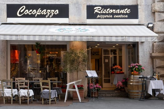 Milan, Italy - April, 08, 2025: Cocopazzo Ristorante storefront in Milan. Italian eatery with outdoor seating, menu stand, flowers and rustic decor.