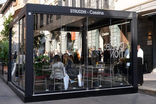 Milan, Italy - April, 08, 2025: Outdoor STRUCCHI and Cassina pop-up lounge at Milan Design Week 2025 with people seated and Cassina store visible behind.