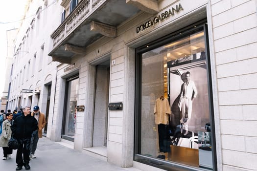 Milan, Italy - April, 08, 2025: Dolce and Gabbana boutique exterior in Milan with fashion display and pedestrians walking by. Luxury retail storefront scene.