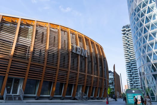 Milan, Italy - April, 08, 2025: IBM Pavilion in Milan. Modern eco-architecture with wooden slats, urban skyscrapers and pedestrians in Porta Nuova district.