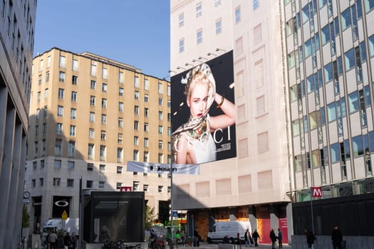 Milan, Italy - April, 08, 2025: Large Gucci fashion campaign billboard on city building facade in Milan near metro entrance. Street view with people walking.