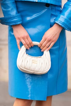 Paris, France - March 11, 2025: Woman wears quilted white Miu Miu mini bag with gold logo, paired. Street style outfit details.