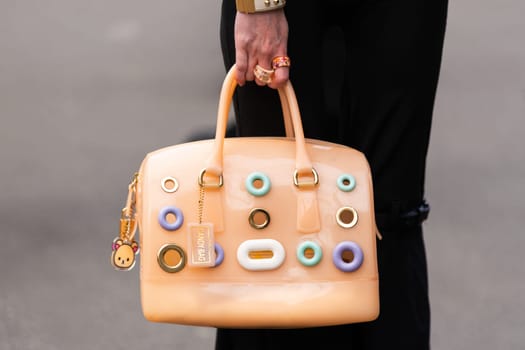 Paris, France - March 11, 2025: Woman wears peach Furla Candy Bag with pastel ring details and bear charm. Street style outfit details.