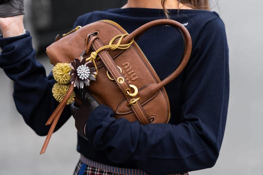 Paris, France - March 11, 2025: Woman wears brown Miu Miu handbag with leather strap, gold hardware and floral charms. Street style outfit details.