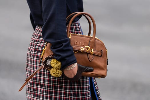 Paris, France - March 11, 2025: Woman wears brown Miu Miu handbag with leather strap, gold hardware and floral charms. Street style outfit details.