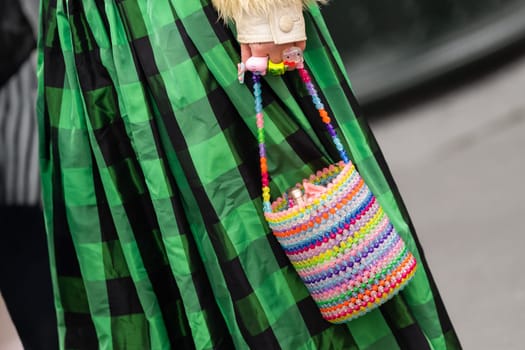 Paris, France - March 11, 2025: Rainbow beaded bucket bag with toys and colorful rings, worn with green check pleated midi skirt. Street style outfit details.