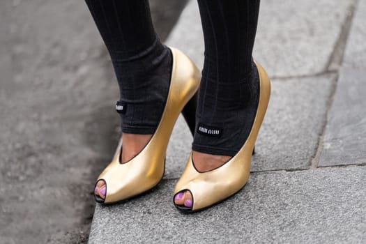 Paris, France - March 11, 2025: Woman wears Miu Miu gold wedge heels, grey socks. Street style outfit details.