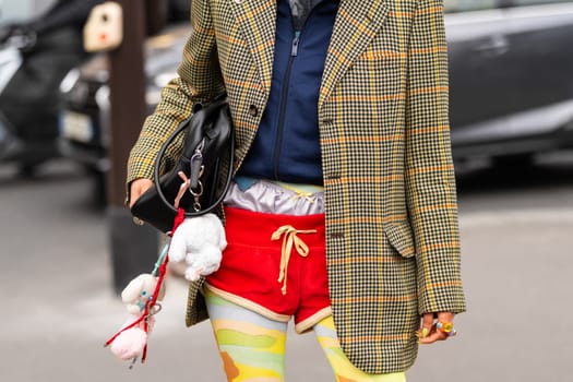 Paris, France - March 11, 2025: Black Loewe Puzzle shoulder bag with plush charms. Red velvet shorts and patterned tights. Street style outfit details.