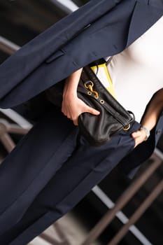 Paris, France - March 11, 2025: Woman wears black Miu Miu clutch bag with gold clasp hardware and yellow envelope. Street style outfit details.