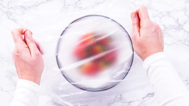 Flat lay. Strawberries, freshly washed and dried, are neatly stored in a glass bowl lined with a paper towel and securely covered with plastic wrap to maintain freshness.