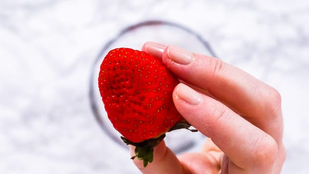 Flat lay. Strawberries, freshly washed and dried, are neatly stored in a glass bowl lined with a paper towel and securely covered with plastic wrap to maintain freshness.