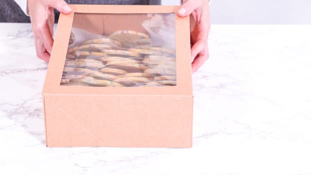 The sugar cookies, filled with sprinkles mixed into the dough, are carefully arranged with meticulous precision into a rustic brown paper box.