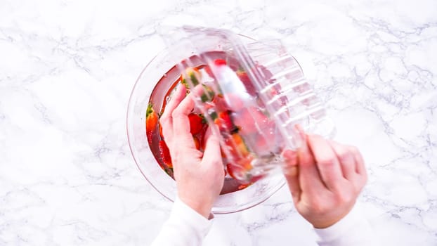 Flat lay. Ripe strawberries are submerged in water within a large glass mixing bowl, a step in washing the fruit to ensure cleanliness and longevity before storage or consumption.