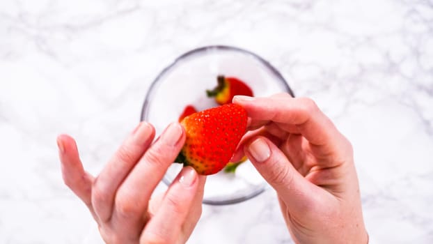 Flat lay. Strawberries, freshly washed and dried, are neatly stored in a glass bowl lined with a paper towel and securely covered with plastic wrap to maintain freshness.