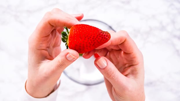 Flat lay. Strawberries, freshly washed and dried, are neatly stored in a glass bowl lined with a paper towel and securely covered with plastic wrap to maintain freshness.