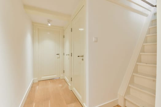 A clean, modern hallway showcasing minimalist design with white walls and wooden flooring, leading to a staircase, creating an airy atmosphere.