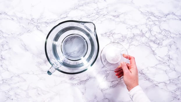 Flat lay. A spacious glass mixing bowl filled with water sits prepared to gently cleanse a batch of ripe strawberries, ensuring they are pristine before drying or storage.
