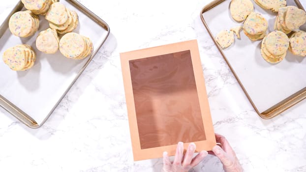 Flat lay. With precision, the woman is carefully arranging the sugar cookies, filled with dough-mixed sprinkles, into a rustic brown paper box.