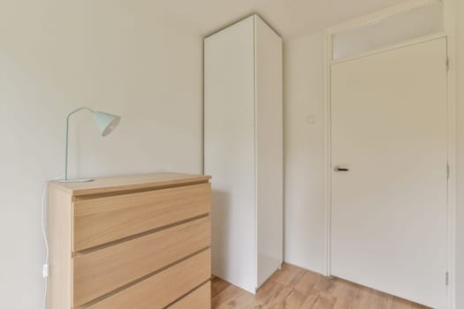 A tidy minimalist bedroom featuring a wooden dresser and a tall white wardrobe against a light background, emphasizing simplicity and elegance.