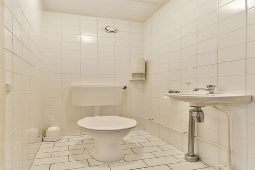 A clean and simple bathroom featuring white tiled walls and floor, with essential fixtures including a toilet and sink in a serene atmosphere.