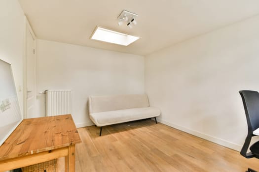Bright, spacious room featuring a sleek sofa, wooden furniture, and natural light through a skylight, emphasizing simplicity and modern aesthetics.
