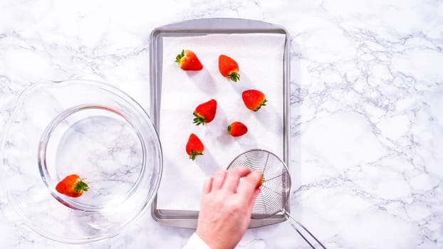 Flat lay. Juicy red strawberries, freshly washed, are spread out to dry on a baking sheet, carefully lined with paper towels to absorb excess moisture and prevent mold.