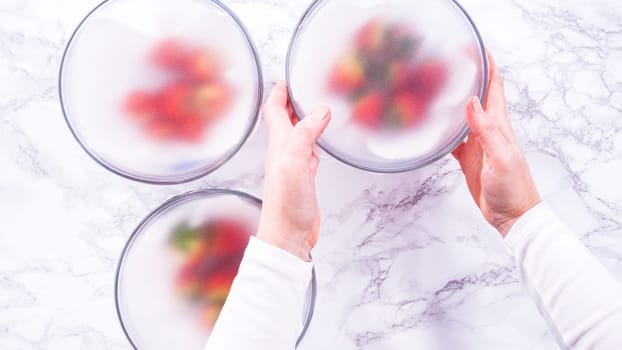 Flat lay. Strawberries, freshly washed and dried, are neatly stored in a glass bowl lined with a paper towel and securely covered with plastic wrap to maintain freshness.