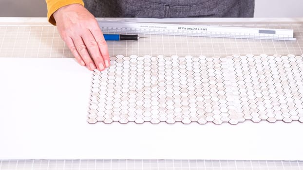 In the process of mounting peel and stick mosaic tiles onto a foam board, perfect for enhancing a food photography studio's aesthetic.
