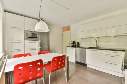 A sleek modern kitchen featuring a minimalist design, complemented by red chairs around a white dining table and contemporary fixtures. A cozy yet stylish atmosphere is created.