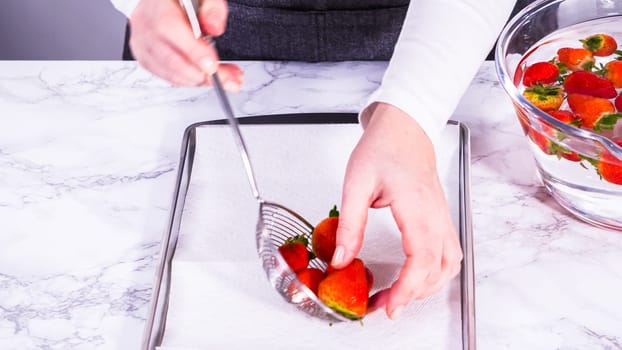 Juicy red strawberries, freshly washed, are spread out to dry on a baking sheet, carefully lined with paper towels to absorb excess moisture and prevent mold.